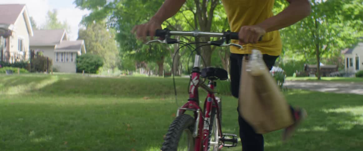 A man parks his bicycle on the lawn to make a delivery