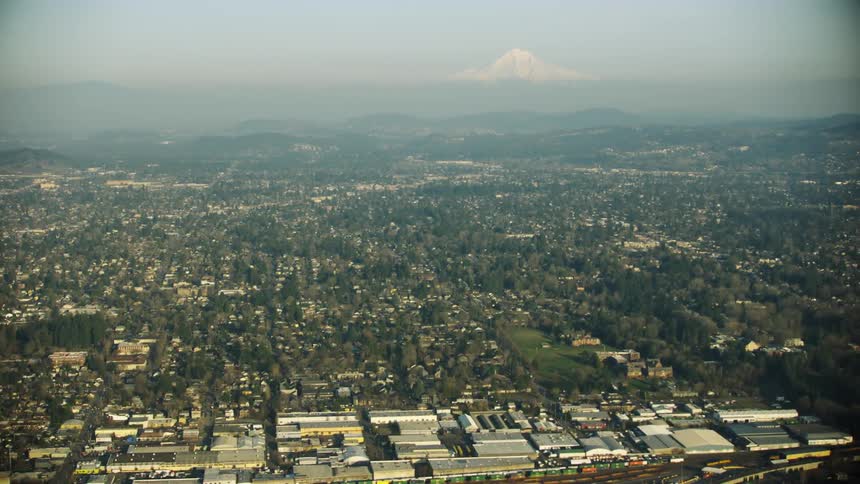 Aerial shot of the vast and sprawling neighborhoods of Portland Oregon with Mount Hood and the Cascade Volcanos towering over the far horizon