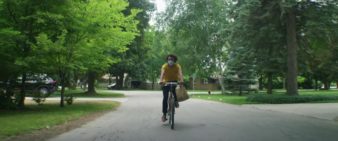 A man rides a bicycle on a neighborhood road carrying a paper bag