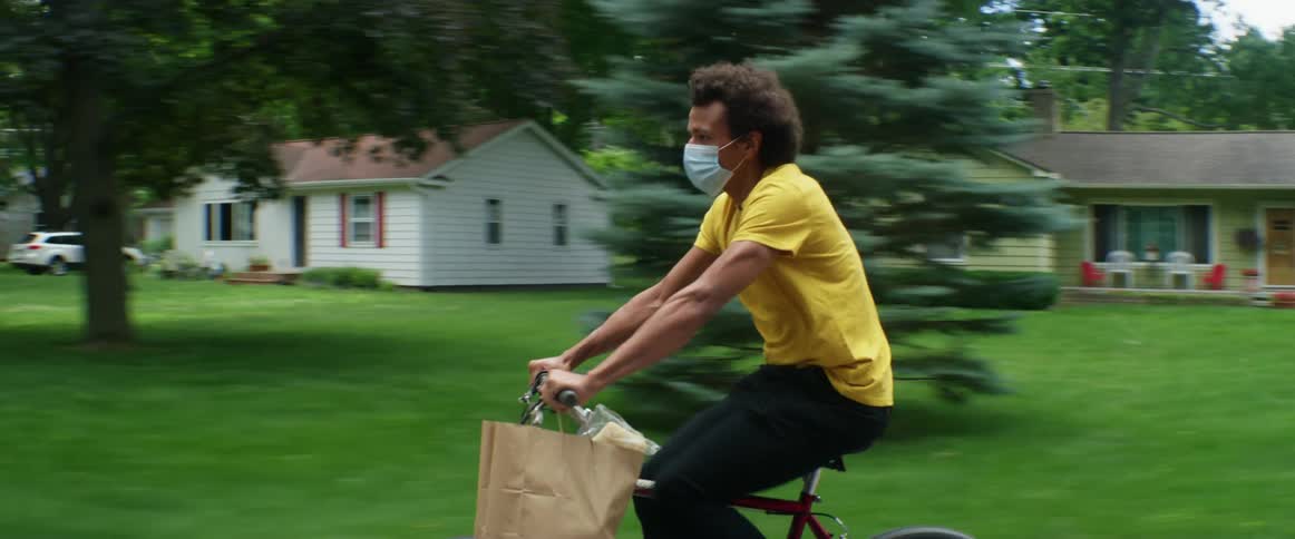 Young man wearing a surgical face mask driving a bicycle on the streets of a neighborhood