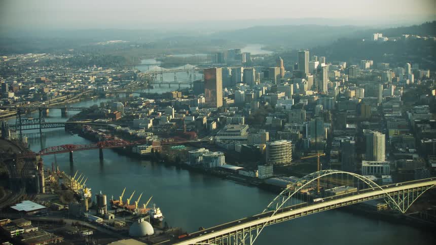 Aerial shot of downtown Portland Oregon flying past the Willamette River looking north at the Steel bridge and eventually revealing the The Fremont Bridge and Interstate 5 crossing the river on a gritty day