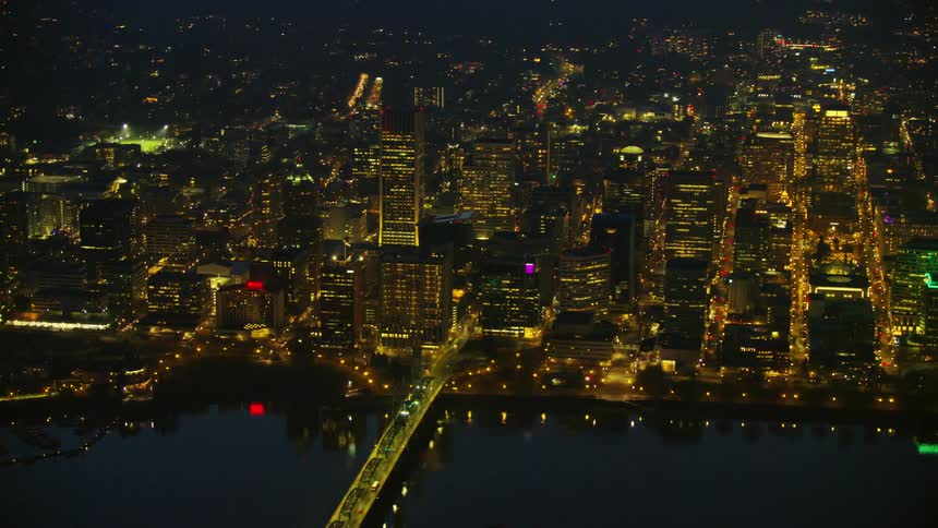 Medium shot night time aerial of downtown Portland Oregon with the Hawthorne Bridge and the Willamette River in the foreground and many skyscrapers in the background