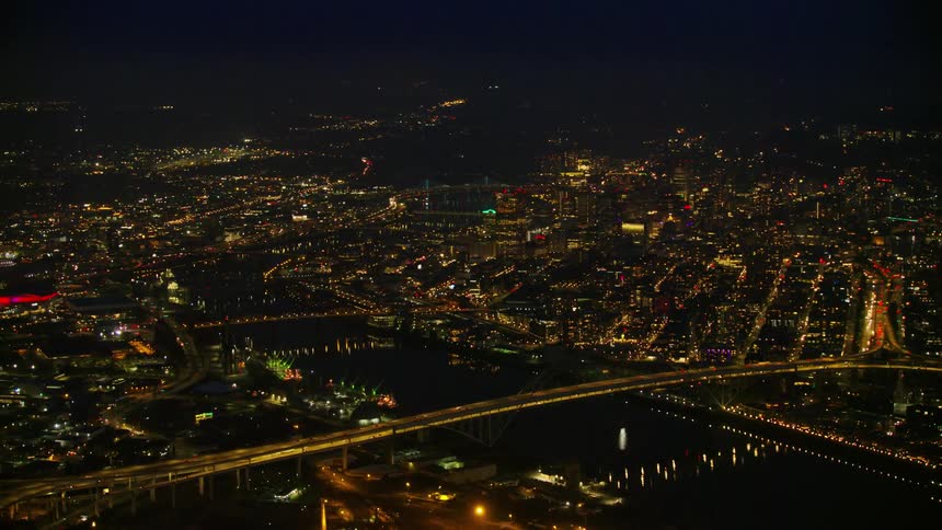 Wide night aerial shot of downtown Portland Oregon and the Willamette River under a dark night sky with beautiful city lights illuminating the scene