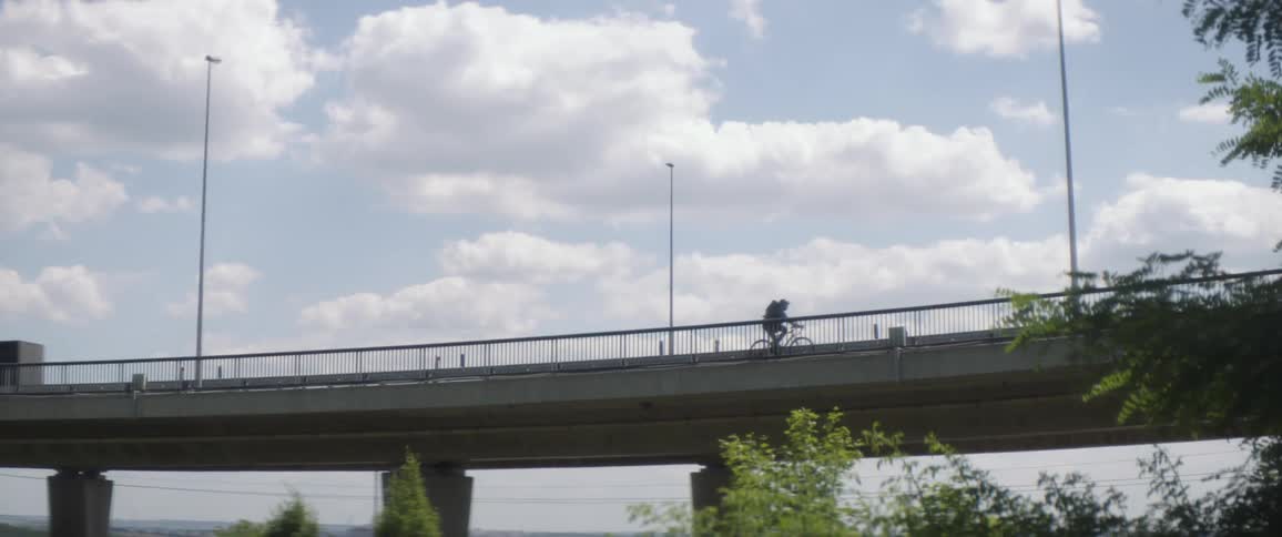 A bicyclist and vehicles traveling on an overpass in the daytime