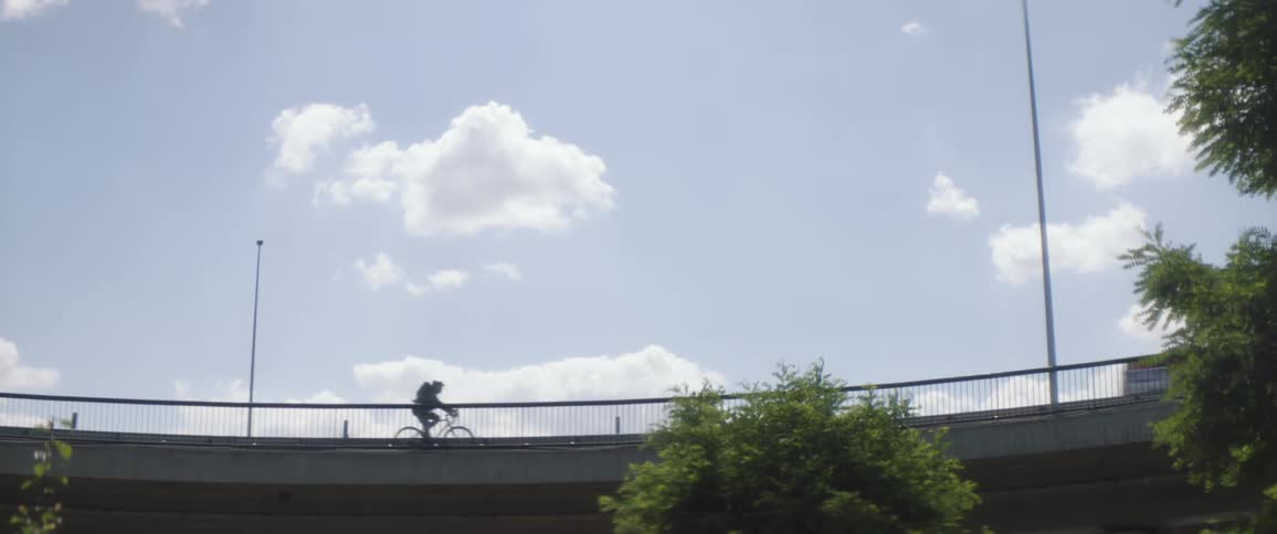 A bicyclist and cars traveling on an overpass in the daytime