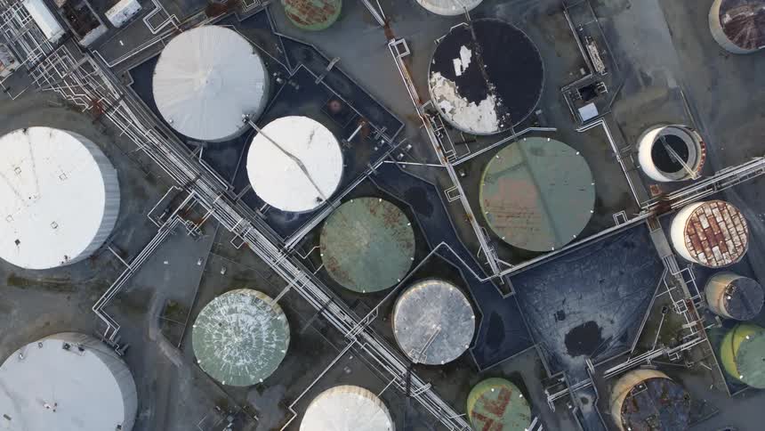 Birds eye twisting descent of corroded oil and chemical tanks