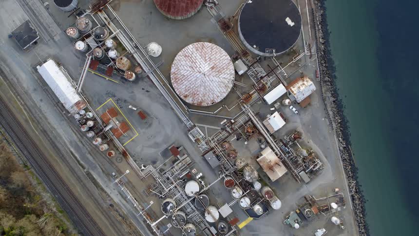 Straight above pipes and old cylindrical storage tanks next to calm ocean water
