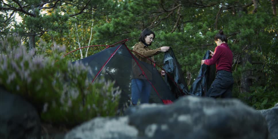 Two women fold a tarp near a tent in the woods