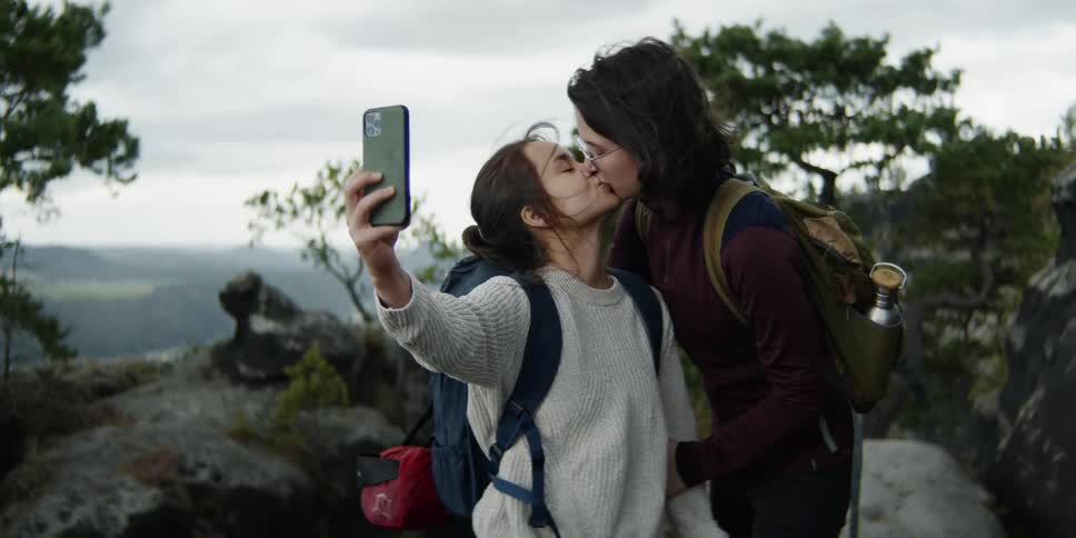 Two girls out hiking take a selfie and kiss
