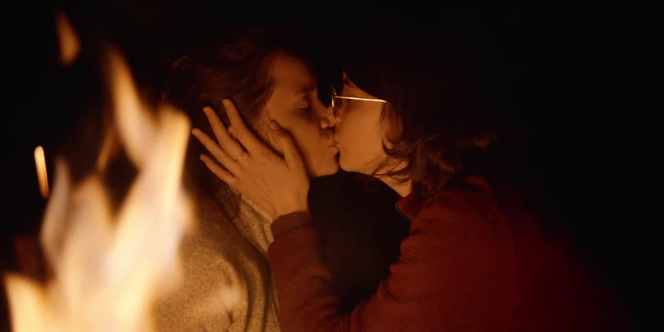 Two teenage girls kiss in front of a fire