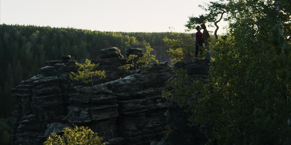 A couple stands outside on a cliff kissing