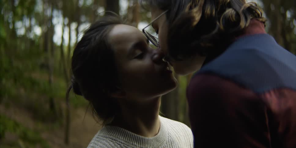 A woman looks up at her female companion before the two of them kiss with passion