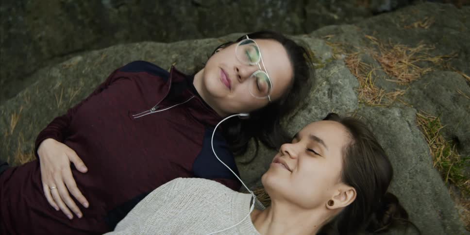 Two teenage girls lying outside on a rock look at one and another and kiss