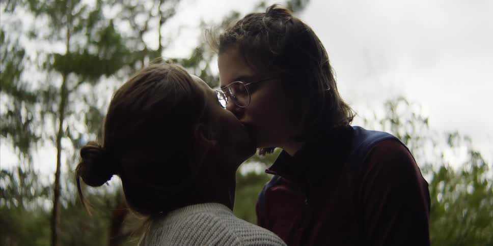 Lesbian couple kisses each other softly in the forest on a cloudy day