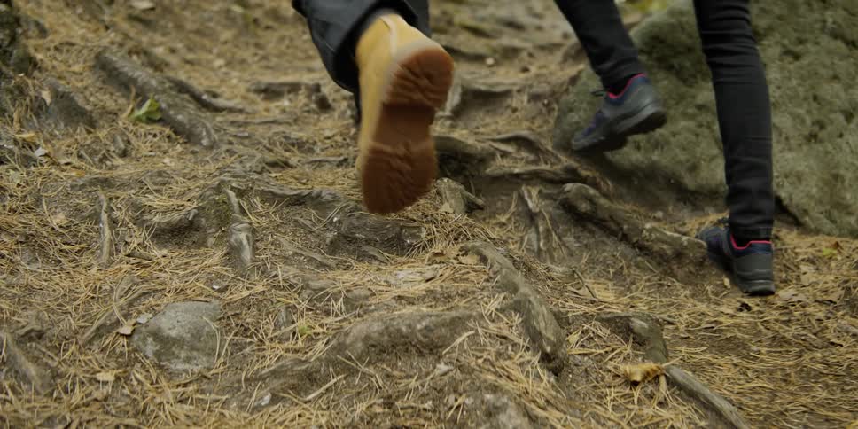 A view of the feet of a man and woman climbing a steep hill in a forest