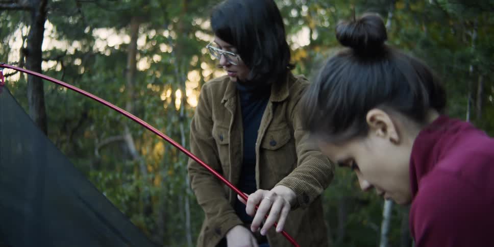 Two teenage girls setting up a tent in a forest
