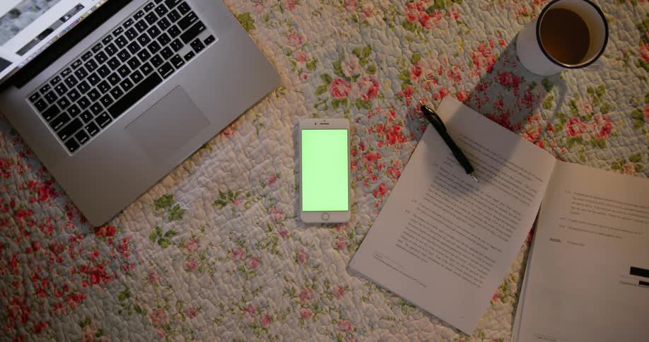 Table holding several items including a smartphone, laptop  pen and paper as well as a drink