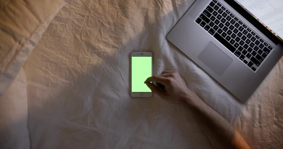 A man uses a laptop and phone in bed
