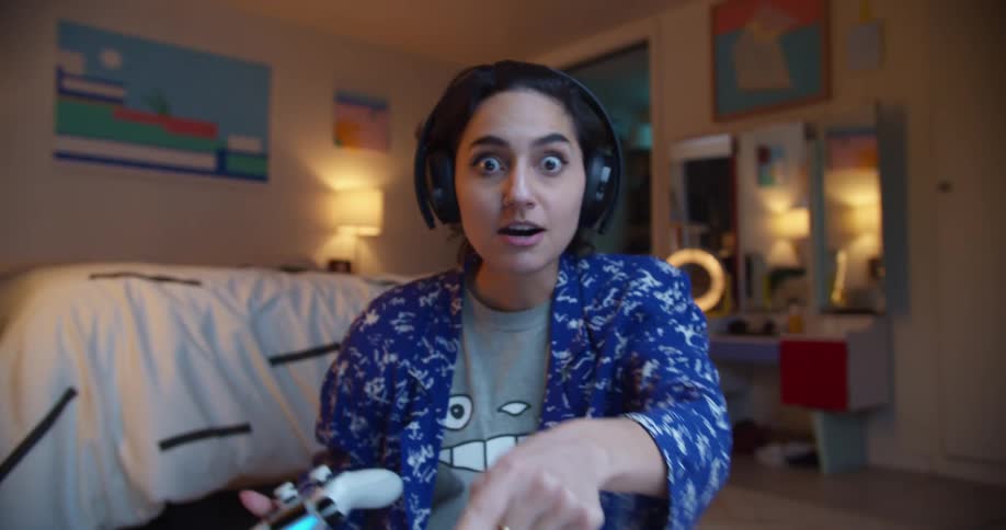 Young woman sitting on the floor in her bedroom plays videogames while looking at the camera