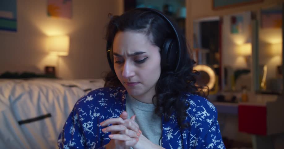 A woman in a room putting on headphones with a mirror and a lamp in the background