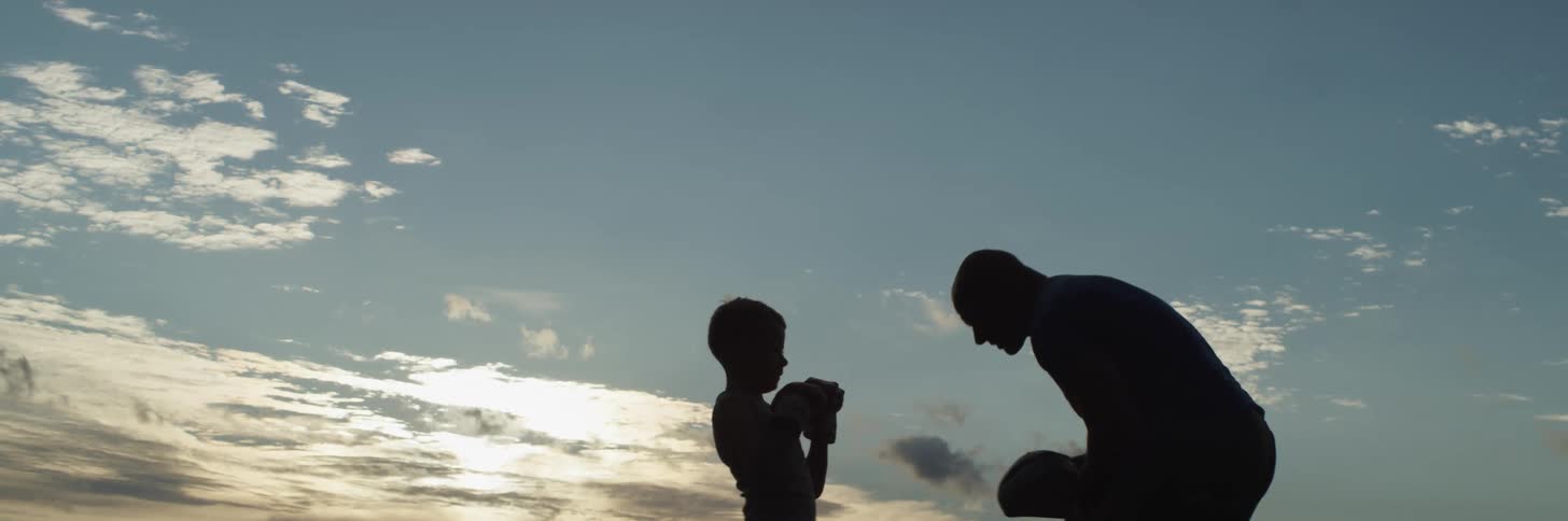 Silhouettes of a man and boy practicing martial arts with the sky and clouds in the background