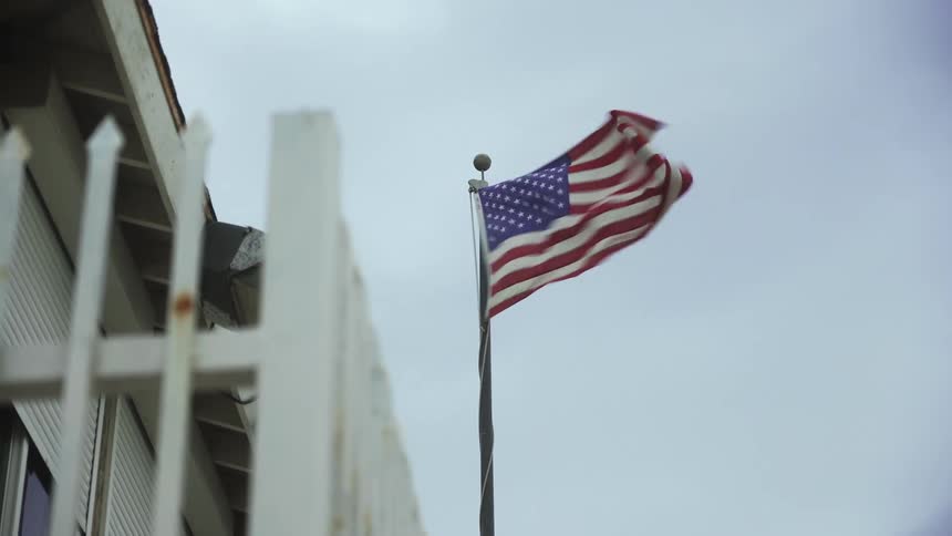 American flag vigorously waving on a flagpole in front of a house
