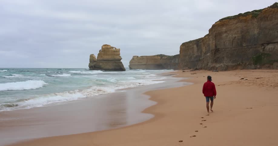 A man walks alone on a beach looking to the ocean water