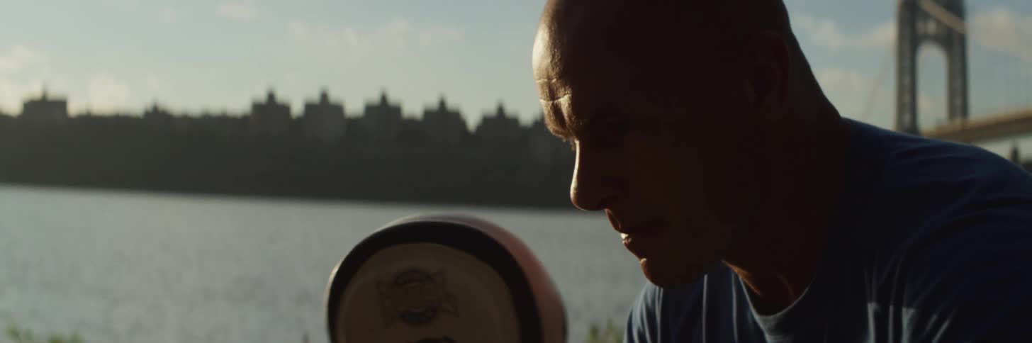 A man with boxing pads standing with grass a river a bridge the sky and clouds in the background