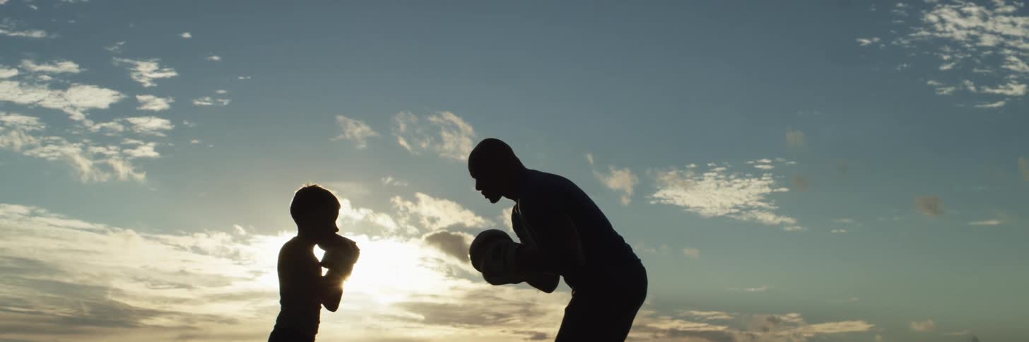 Sillouethe of father teaching son how to box at sunset