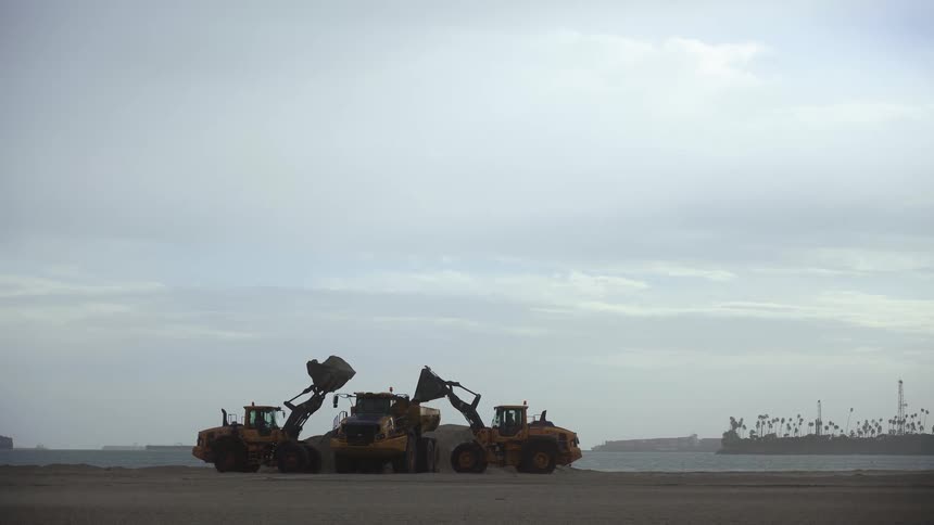 Two bulldozers moving sand on a beach