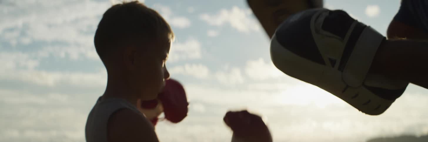 A father is teaching his son how to box outdoors at dusk