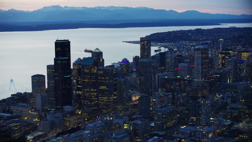Downtown Seattle is in the foreground and the Puget Sound and Olympic Peninsula in the background as the aerial shot wraps around the city