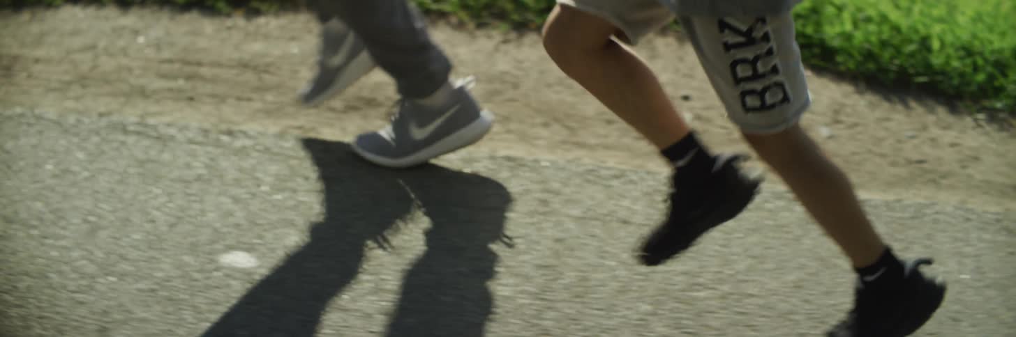 Two people running with sneakers with grass and a body of water in the background