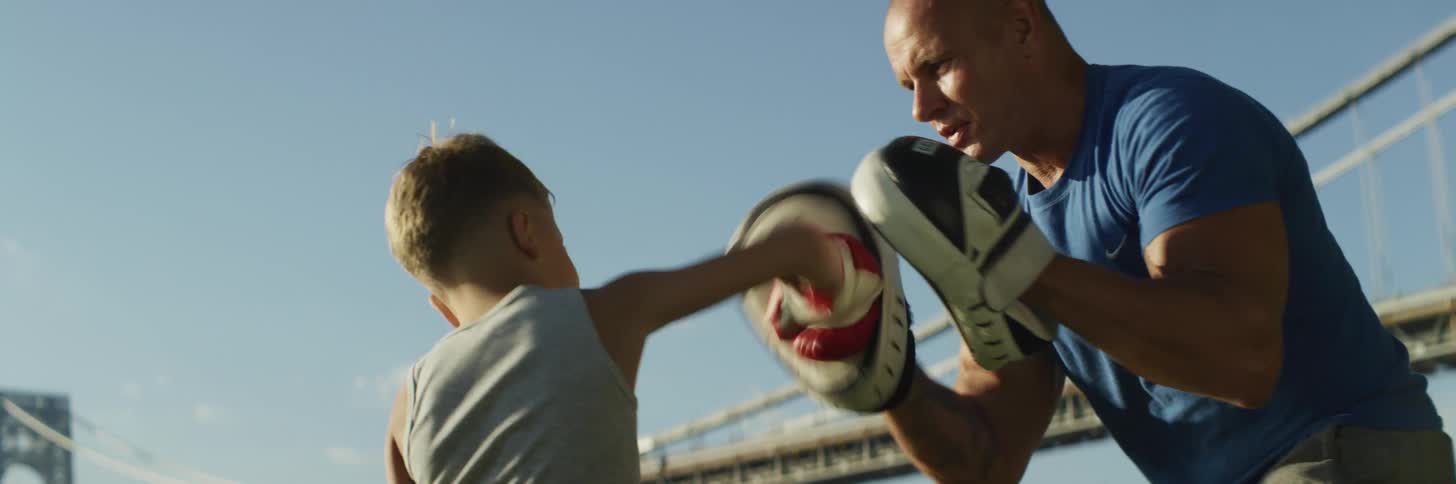 Man trains boxer standing outdoors near suspension bridge