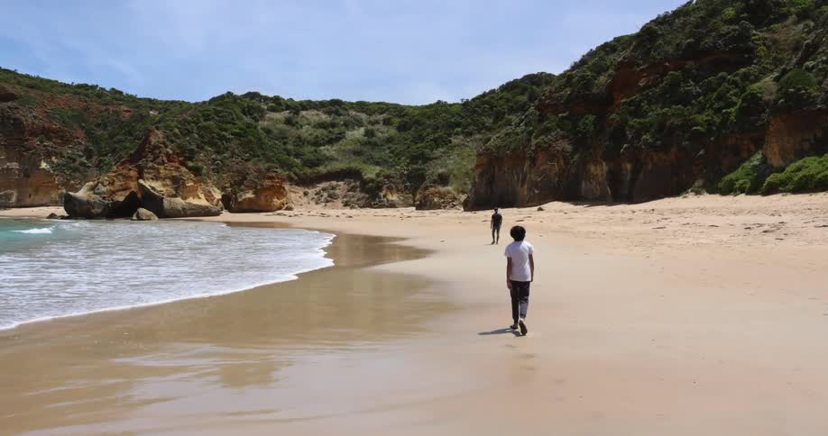 Two young men walking on the sand of a beach near the hills