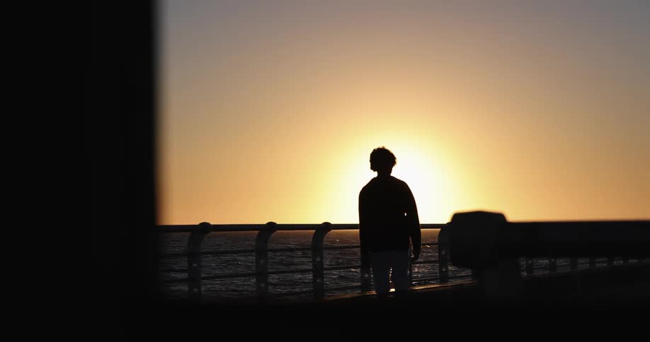 The silhouette of a person walking along a waterfront at sunset