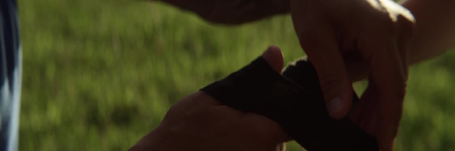 A man wraps a long black bandage around his sons wrist and hand as they stand outside