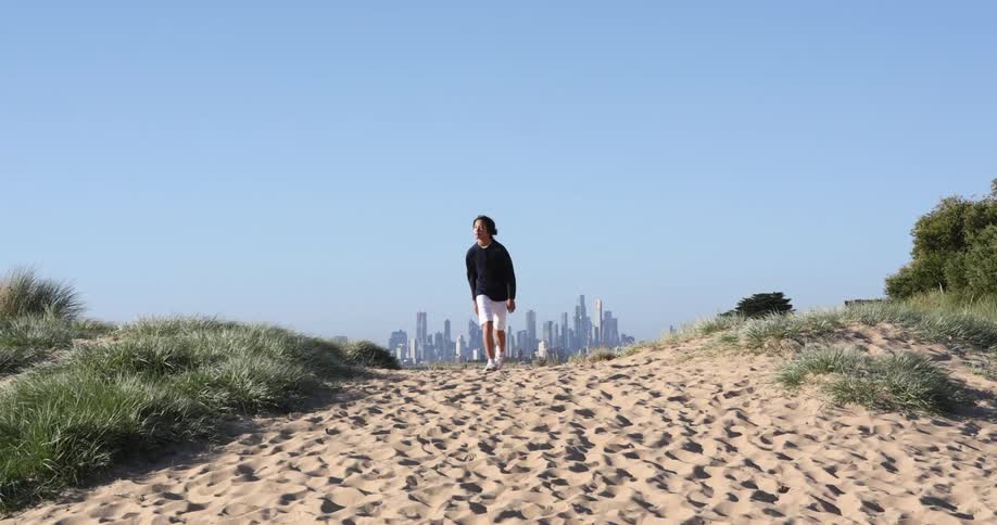 A person walking on sand with a city skyline the sky and clouds in the background