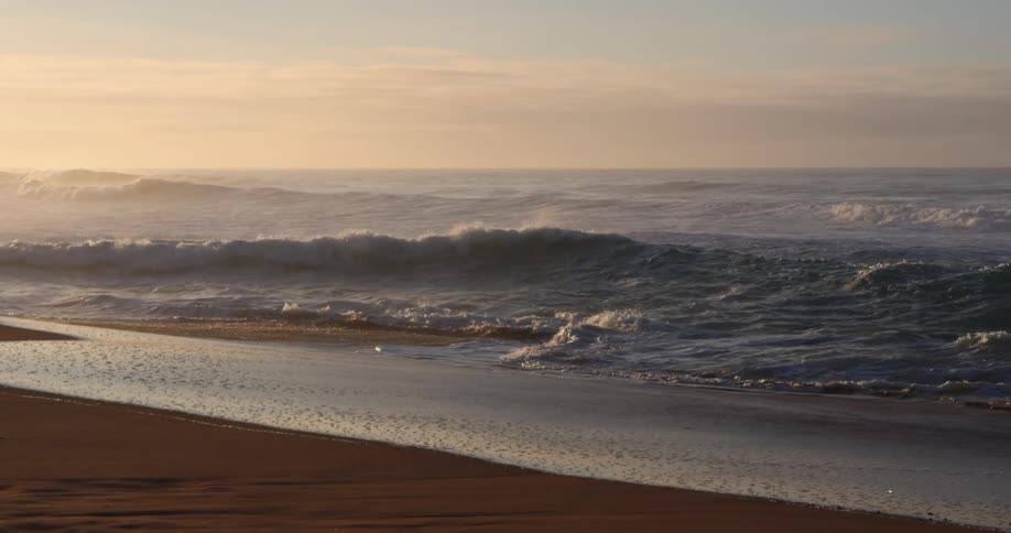 Ocean waves wash onto a sandy beach in the evening