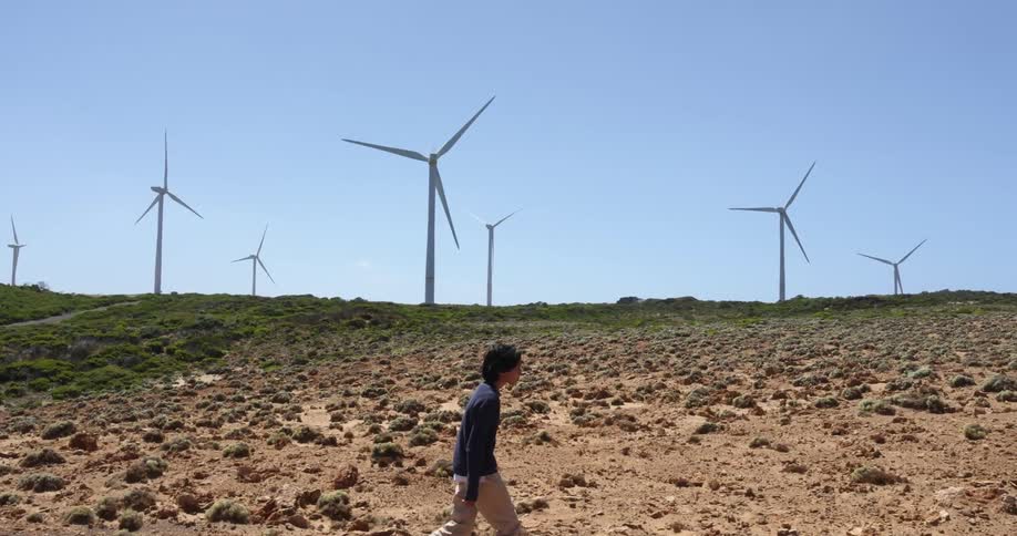 A teenager walks along a hill lined with wind turbines