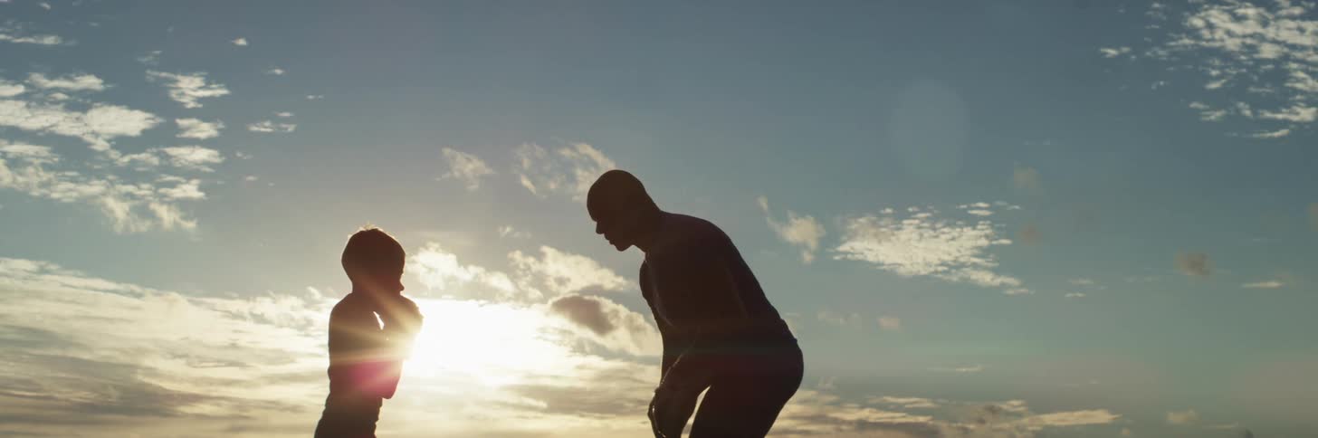The silhouette of a dad training with his son outside using boxing pads and gloves