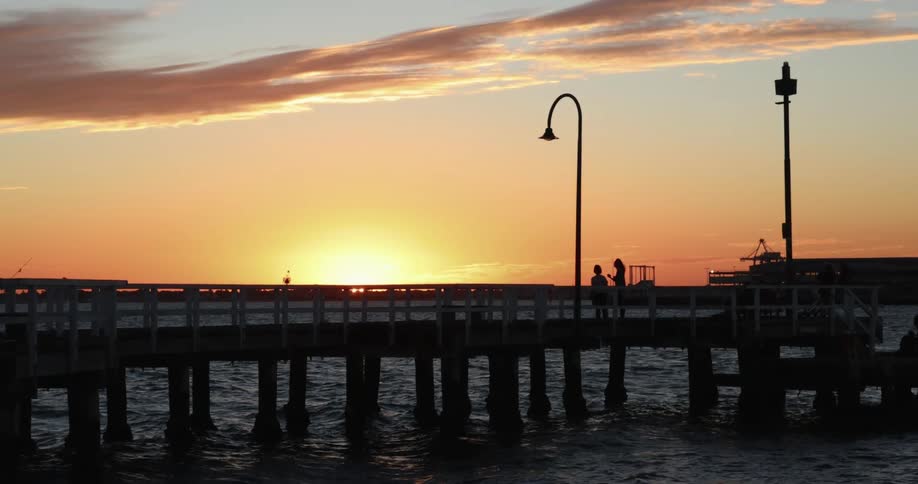 Two people stand on a dock as the sun sets