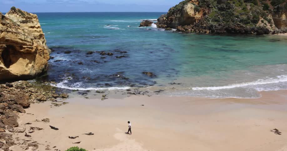 A man walks alone on the beach toward a line of boulders