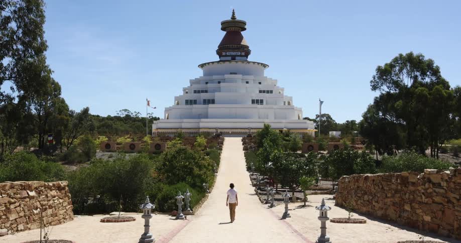 A person walking on a pathway to a building surrounded by trees with the sky and clouds in the background