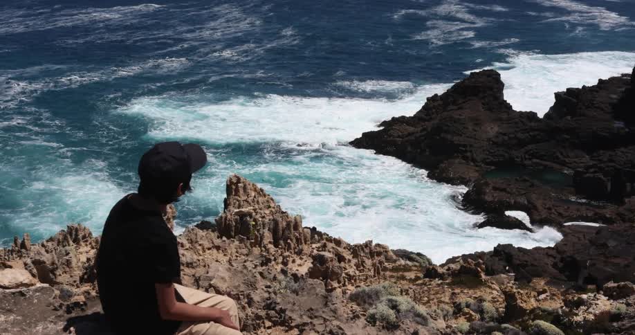 A person is sitting on the rocks watching the water