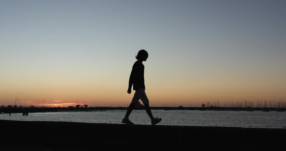 A silhouette of a person walking with a lake the sky and clouds in the background