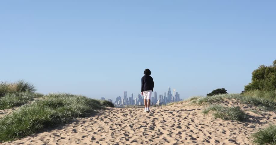 A person walking over a sand dune towards the city skyline