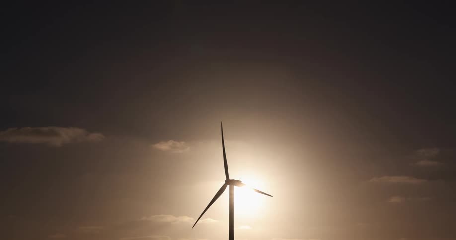 A single wind turbine blows in the wind as the sun is directly behind it