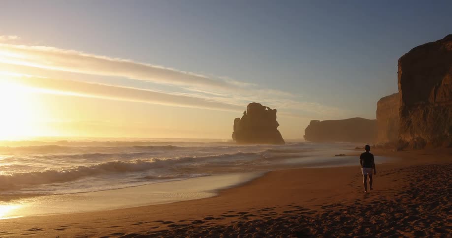A person is walking on the beach at sunrise