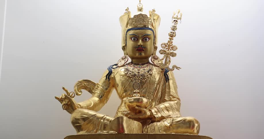 Ornate very detailed gold statue sits against pale background under bright light source